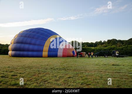 Ein Heißluftballon. Vor dem Start den Ballon (oder Umschlag) mit Luft füllen. Morgenaufgang auf einem Feld. Stockfoto