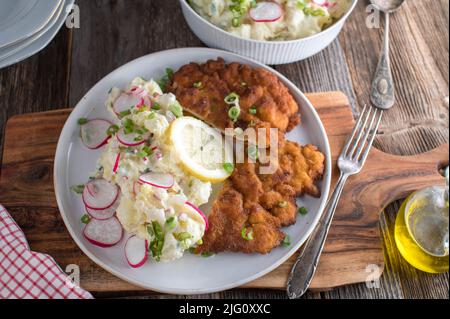 Deutsches Komfortessen mit einem frischen, panierten Schweinefleisch-Schnitzel in der Pfanne. Serviert mit hausgemachtem Kartoffelsalat auf einem Teller Stockfoto