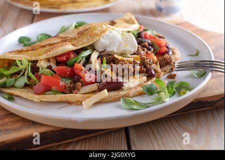 Hackfleischgericht mit einem frischen Pfannkuchen oder Crepe, gefüllt mit Kidney Beans, Gemüse, Käse und mit saurer Rahm gekrönt Stockfoto