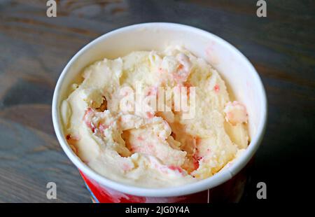 Köstliches Erdbeer-Banane-Eis in einer großen Tasse auf schwarzem Holztisch Stockfoto