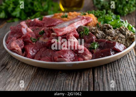 Rohfleischfütterung für Hunde. Ein Teller mit frischem Muskelfleisch, Knochen, Pansen, Innereien, Gemüse und Kräutern Stockfoto