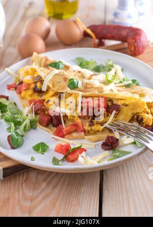 Herzhaftes Frühstück mit hausgemachtem, gebackenem Crepe, gefüllt mit Rührei, Chorizo-Wurst, Käse und Tomaten. Stockfoto