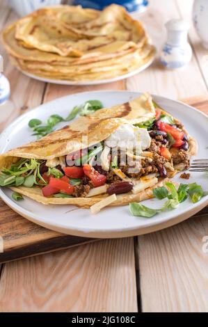 Herzhaftes Pfannkuchengericht oder Crepe, gefüllt mit würzigem Hackfleisch, Kidney Beans, Gemüse und Käse. Garniert mit saurer Creme Stockfoto