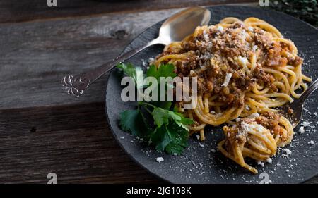 Spaghetti Bolognese auf einem dunklen Teller auf einem Holztisch Stockfoto