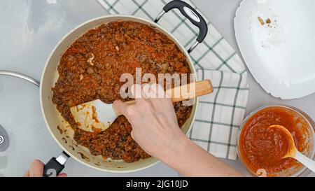 Frau mischt Hackfleisch und Marinara-Sauce in der Pfanne. Nahaufnahme des Kochvorgangs. Schritt für Schritt Rindfleisch Lasagne Rezept Stockfoto