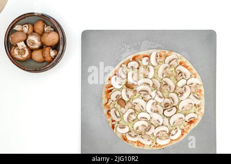 Rohe Pizza mit Tomatensauce, Mozzarella-Käse und Crimini-Pilzen in Nahaufnahme auf Backform auf weißem Hintergrund, Platz kopieren Stockfoto