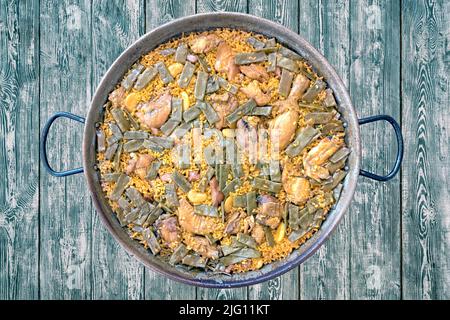 Ursprüngliche valencianische Paella aus Reis, Huhn, Kaninchen, grünen Bohnen, der traditionellen Bohne namens "Garrofón". Die Paella wird auf einen Holztisch gestellt Stockfoto