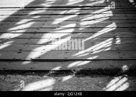 Eine schwarz-weiße Nahaufnahme von Schatten und Licht auf einem Steg. Stockfoto