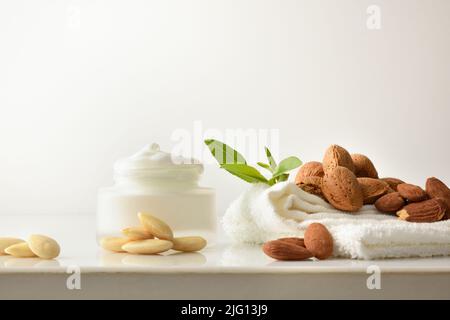 Mandelcreme Hautpflege mit Fruchthandtuch und Blättern auf weißem Tisch und weißem isoliertem Hintergrund. Vorderansicht. Horizontale Zusammensetzung. Stockfoto