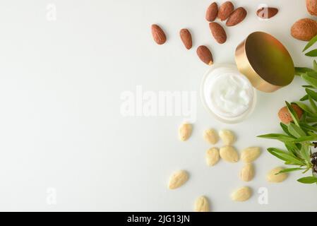 Mandelcreme Hautpflege mit Früchten und Blättern auf weißem Tisch und weißem isoliertem Hintergrund. Draufsicht. Horizontale Zusammensetzung. Stockfoto
