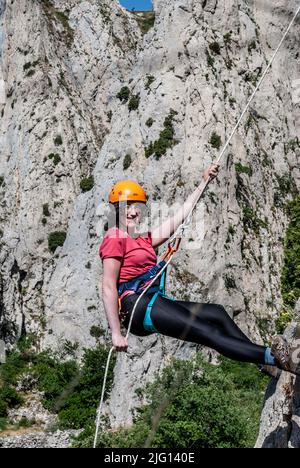 Schöne Frau klettert auf hohen Felsen bei Sonnenuntergang Nebel in den Bergen. Konzept von Abenteuer und Extremsport Stockfoto