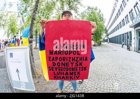 6. Juli 2022, München, Bayern, Deutschland: Ein Demonstrator in München hält ein Schild mit den Namen einiger der bekannten gefallenen Städte im russischen Krieg gegen die Ukraine. Als Reaktion auf das Treffen von Bundesfinanzminister Robert Habeck mit der Lobbygruppe des Vereins der Bayerischen Wirtschaft demonstrierten die Ukrainer in München draußen für eine Gas- und Energiepolitik, die der Bedrohung, die Putin für die Ukraine und Europa darstellt, angemessen ist. Die Demonstranten fordern einen Stopp der Energiebeschaffung aus Russland, bevor Putin die Lieferungen an ein unvorbereitetes Europa, gegen das sie kämpfen, unterbricht Stockfoto