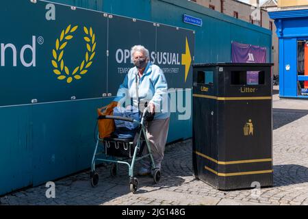 1. Juli 2022. High Street, Elgin, Moray, Schottland. Dies ist eine ältere Bürgerin auf der Straße mit ihrem Push cahir und trägt eine Schutzmaske. Stockfoto