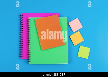 Bunte Schreibwaren isoliert auf blauem Hintergrund. Stapel von Notizbüchern und Haftnotizen in verschiedenen Farben, Draufsicht. Stockfoto