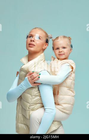 Virtuelle Technologie. Glücklich entzückt nettes Mädchen lächelnd und Blick auf die Kamera, während Mutter in ihren Armen in der digitalen virtuellen Brille auf blau gehalten Stockfoto