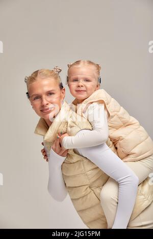 Virtuelle Technologie. Glücklich erfreut nettes Mädchen lächelnd und Blick auf die Kamera, während Mutter in ihren Armen in digitalen virtuellen Brille auf der Bienge hält Stockfoto
