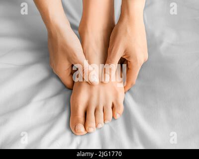 Eine Frau massiert ihren Fuß, während sie im Bett sitzt. Nahaufnahme. Stockfoto