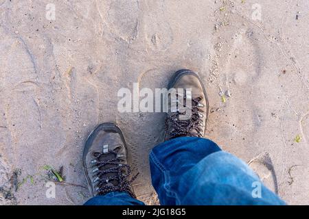 Der Mann in Stiefeln und blauen Jeans läuft am nassen Sand des Meeresstrandes entlang Stockfoto