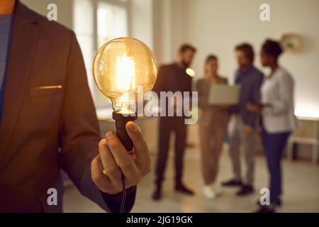 Glühbirne, die von einem Geschäftsmann vor dem Hintergrund eines kreativen Geschäftsteams gehalten wird. Stockfoto
