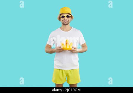 Ein junger, positiver Kaukasusmann mit Sonnenbrille hält die gelbe Ente für Schwimmstände im Studio Stockfoto