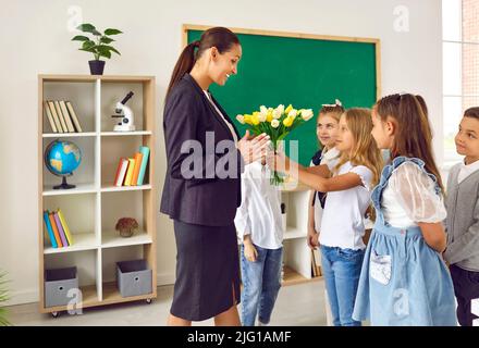 Schüler gratulieren ihrer Lehrerin und schenken ihr im Klassenzimmer Blumen. Stockfoto