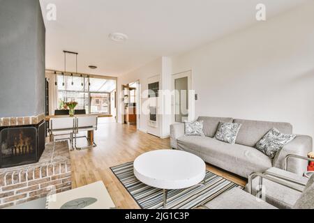 Stilvolles, luxuriöses Wohndesign mit gemütlichem Wohnzimmer mit Kamin und komfortablem Sofa und Teppich bei Tageslicht Stockfoto