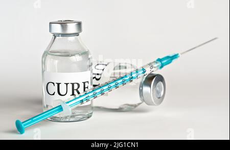 Glas-Impffläschchen mit Etikett Cure auf weißem Brett, blaugrüne Unterspritze nahe - Impfkonzept Stockfoto