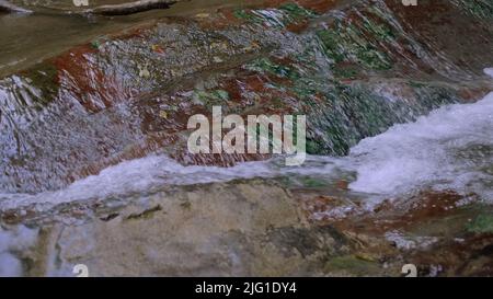 Leichtes Wasser aus der Nähe.Kreativ.Ein kleiner Wasserfall, der die Steine mit klarem Wasser und leicht sprudelnd hinunterfließt. Hochwertige 4K-Aufnahmen Stockfoto