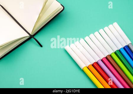 Mehrere Buntstifte auf einem Notizbuch auf einem grünen Tisch. Zurück zur Schule. Stockfoto