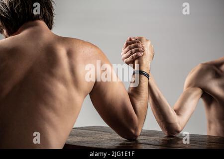 Armdrücken. Stark muskulös bärtigen Mann Arm Ringen ein mickrigen schwachen Mann. Arme ringen dünne Hand, großer starker Arm im Studio. Zwei Männerhände umklammten Stockfoto