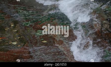 Leichtes Wasser aus der Nähe.Kreativ.Ein kleiner Wasserfall, der die Steine mit klarem Wasser und leicht sprudelnd hinunterfließt. Hochwertige 4K-Aufnahmen Stockfoto