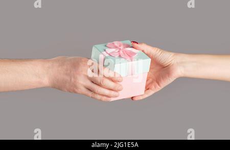 Geschenkbox in der Hand, Überraschung und Urlaubskonzept. Mann Hände halten Valentinstag Geschenk. Männliche und weibliche Hände halten rosa Geschenkbox. Mädchen gibt ein Geschenk Stockfoto