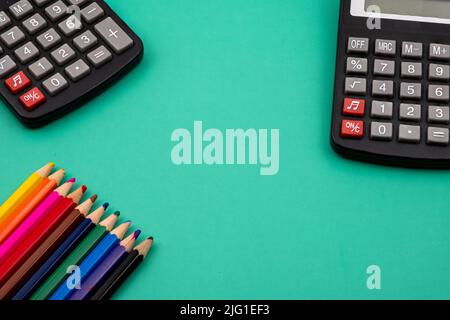 Nahaufnahme eines Bündels Buntstifte und schwarzer Taschenrechner auf einem grünen Tisch. Stockfoto