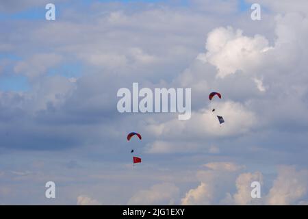 Drei Fallschirmspringer am bewölkten Himmel ziehen Flagge, Banner und Poster von Atatürk für eine Airshow in der Türkei Stockfoto