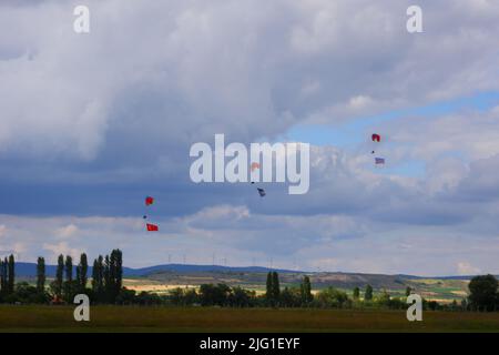 Drei Fallschirmspringer am bewölkten Himmel ziehen Flagge, Banner und Poster von Atatürk für eine Airshow in der Türkei Stockfoto