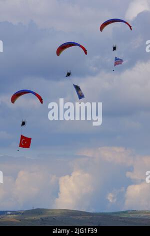 Drei Fallschirmspringer am bewölkten Himmel ziehen Flagge, Banner und Poster von Atatürk für eine Airshow in der Türkei Stockfoto