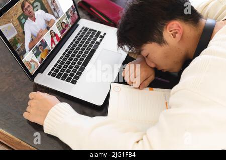 High-Angle-Ansicht des asiatischen Teenagerjungen schlafen vor dem Laptop während Online-Vortrag zu Hause Stockfoto