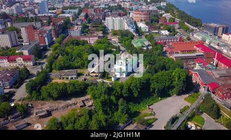 Luftaufnahme eines sommerlichen Stadtteils mit einer Kirche und Häusern. Clip. Schöne grüne Stadt am langen Fluss Stockfoto