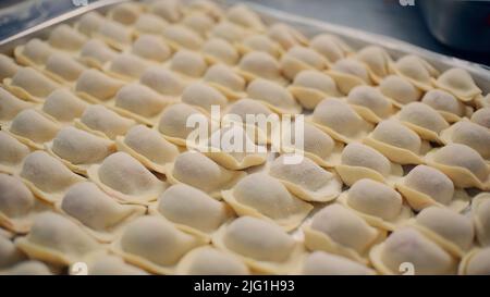 Produktion von russischen Knödeln in einer Fabrik. Clip. Zubereitete Fleischknödel oder Pelmeni liegen in Reihen Stockfoto