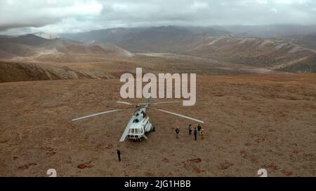 Konzept des Tourismus. Clip. Hubschrauber landete in der Nähe der Gruppe von Menschen in der wilden Region mit dem Tal und den Bergen Stockfoto