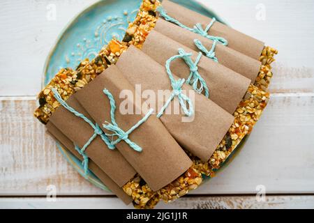 Gesunde Müsliriegel mit Nüssen, Samen und getrockneten Früchten auf einem blauen Teller auf weißem Holzgrund. Vorderansicht , mit Kopierplatz. Stockfoto