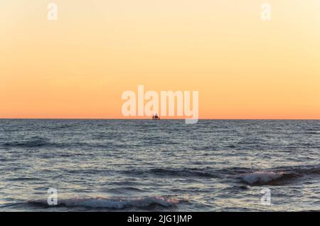 Ein Schiff, das während des Sonnenuntergangs am Horizont segelt Stockfoto