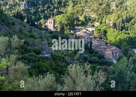 Historische Gebäude und eine Kirche umgeben von üppiger Vegetation in Saint-Guilhem-Le-Désert, Lodève, Frankreich Stockfoto