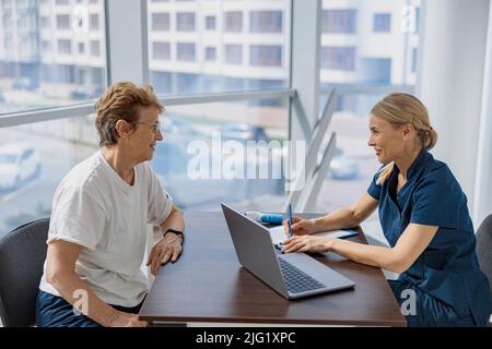 Lächelnder Arzt füllt das Formular für medizinische Berichte über die medizinische Versorgung von Patienten während der Verabredung aus Stockfoto