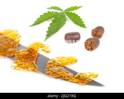 goldenes Wachs auf einem Messer und ein grünes Cannabisblatt mit Hashstücken auf weißem Hintergrund. Stockfoto