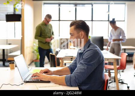 Seitenansicht des kaukasischen jungen Geschäftsmannes, der im Kreativbüro am Laptop arbeitet Stockfoto