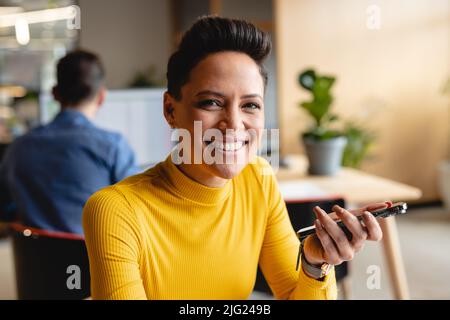 Porträt einer selbstbewussten jungen Geschäftsfrau, die im kreativen Büro ein Smartphone hält Stockfoto