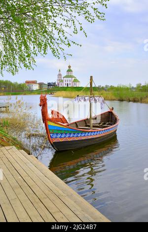 Touristenboot am Pier. Drakkar auf dem Fluss, Elijah Kirche am Horizont, Architektur des XVIII Jahrhunderts. Susdal, Russland, 2022 Stockfoto