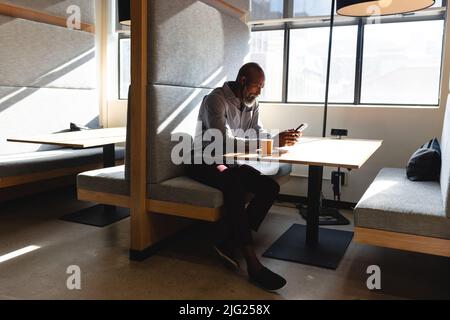 afroamerikanischer reifer Geschäftsmann, der während der Büropause ein Mobiltelefon verwendet Stockfoto