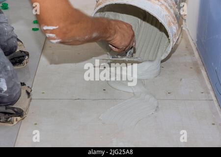 Der Klebstoff auf dem Badezimmerboden wird auf den nassen Mörtel gesprüht, bevor Fliesen aufgetragen werden Stockfoto